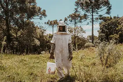 A smiling beekeeper standing in a sunny field.