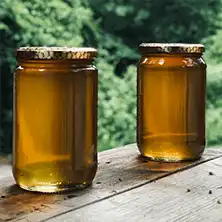 Two jars of clear golden honey sitting on a wooden table.